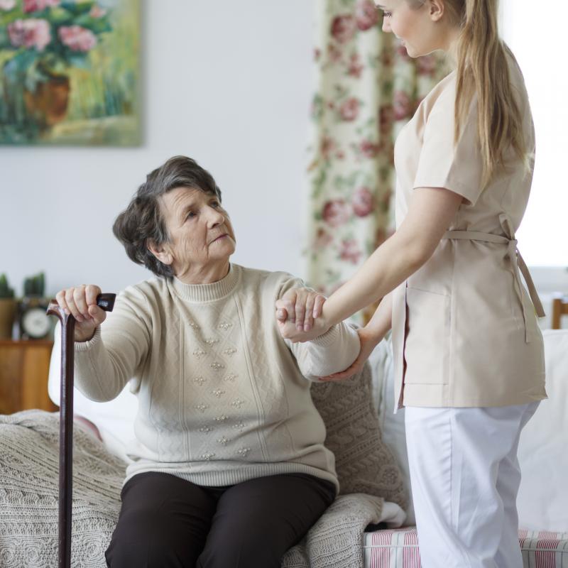 Een jonge vrouw in de thuiszorg helpt een oudere vrouw met opstaan