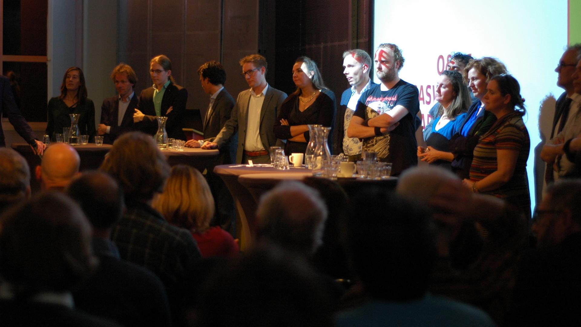 De kandidaten op een rij. Vlnr: Corinne Ellemeet, Bart Snels, Hans Kuipers, Paul Smeulders, Arno Bonte, Isabelle Diks, Huib van Essen, Huub Bellemakers, Zihni Özdil, Suzanne Kröger, Kathalijne Buitenweg, Janet Duursma en Wim-Jan Renkema.  